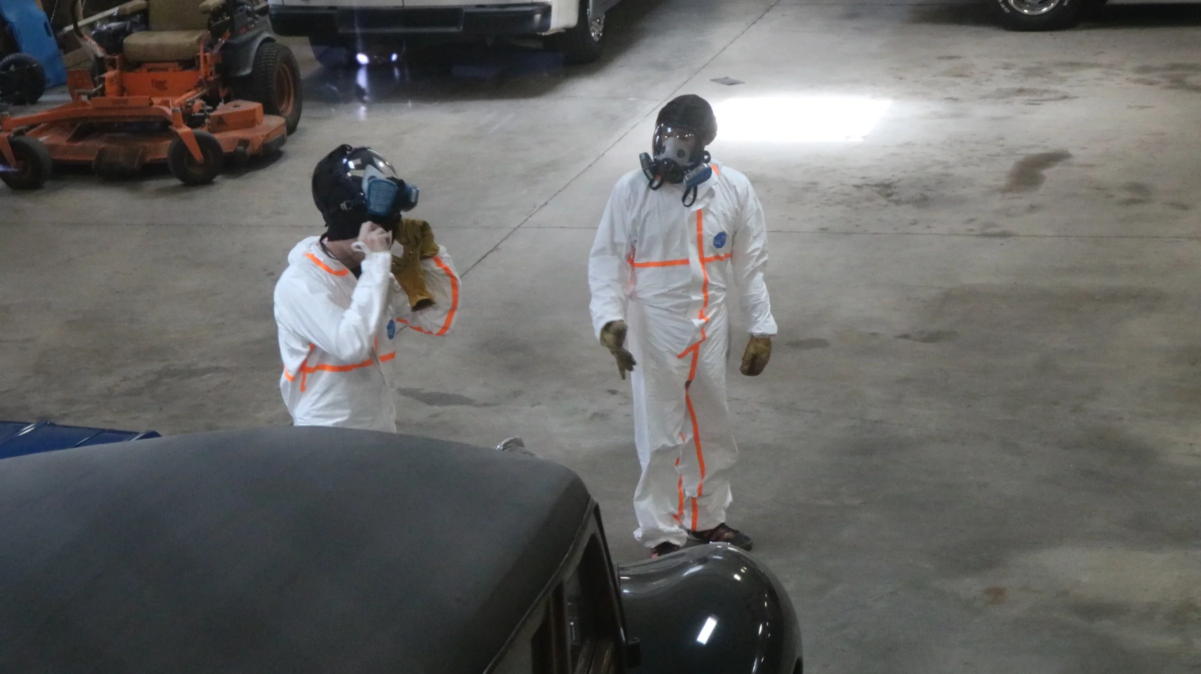 Two builders in protective clothing and respirators at work in a garage workspace.